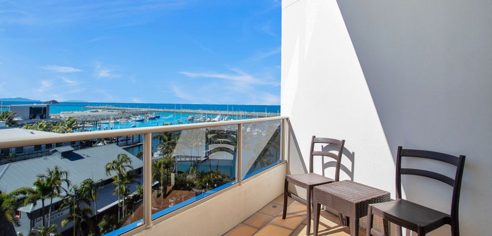 Balcony View – A balcony with a table and two chairs overlooking a peaceful landscape of water and greenery.