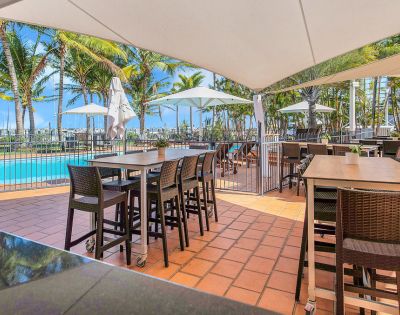Poolside Dining – An outdoor dining area beside a swimming pool with tables and high chairs under a canopy.