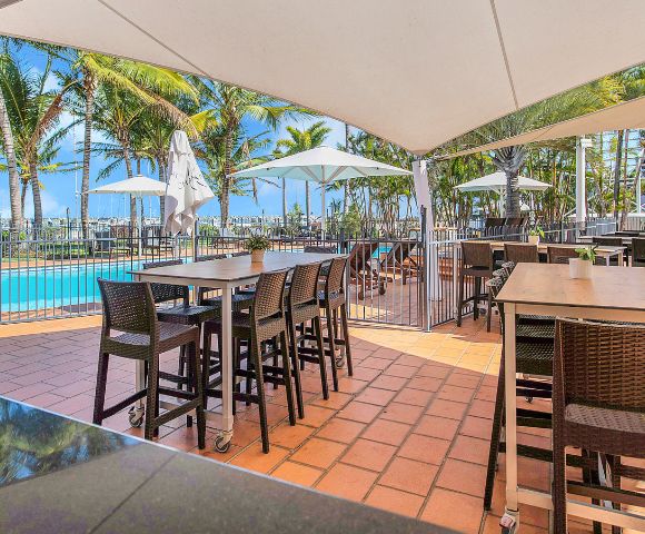 Poolside Dining – An outdoor dining area beside a swimming pool with tables and high chairs under a canopy.