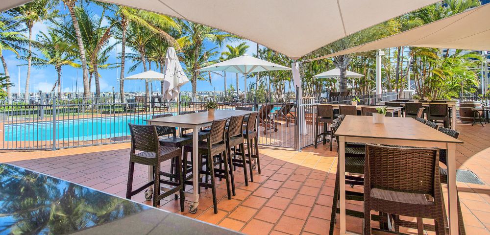 Poolside Dining – An outdoor dining area beside a swimming pool with tables and high chairs under a canopy.
