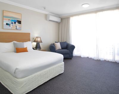 Hotel Room Interior – A simple hotel room with a bed, bedside table, lamp, and a large curtained window.