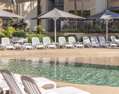Row of white lounge chairs next to a swimming pool with umbrellas in the background.