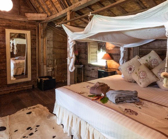 Luxurious bedroom featuring a large bed, wooden walls, and an open window with a view of greenery.