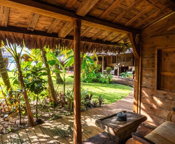 Outdoor seating area under a wooden roof with views of lush tropical greenery.