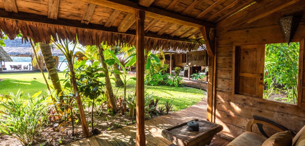 Outdoor seating area under a wooden roof with views of lush tropical greenery.