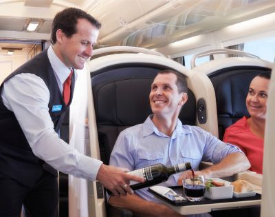 Airplane interior showing two passengers, one being served food by a flight attendant.