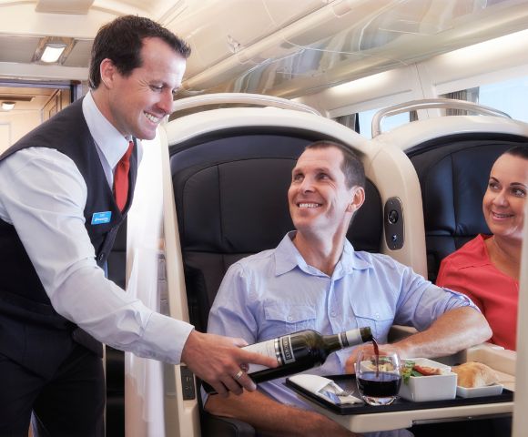 Airplane interior showing two passengers, one being served food by a flight attendant.