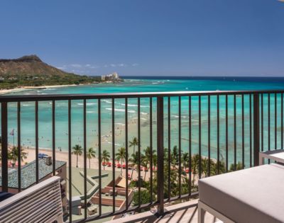 A scenic ocean view from a balcony with clear turquoise water and Diamond Head crater in the background under a bright blue sky.