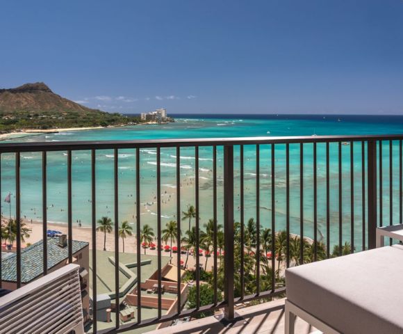 A scenic ocean view from a balcony with clear turquoise water and Diamond Head crater in the background under a bright blue sky.
