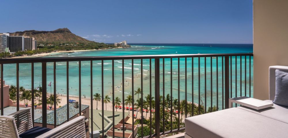 A scenic ocean view from a balcony with clear turquoise water and Diamond Head crater in the background under a bright blue sky.