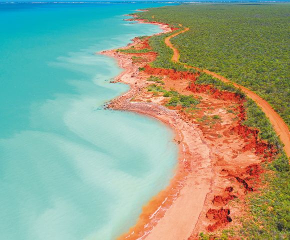 Aerial view of a rugged coastline with turquoise waters and striking red cliffs.