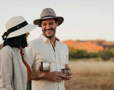 Two people outdoors, one holding a drink, with a scenic natural landscape in the background.