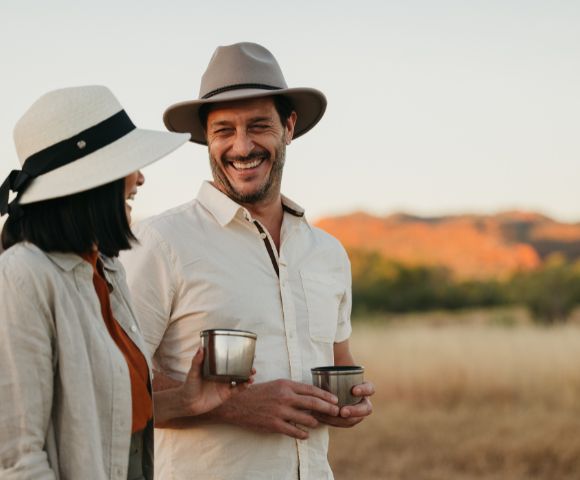 Two people outdoors, one holding a drink, with a scenic natural landscape in the background.