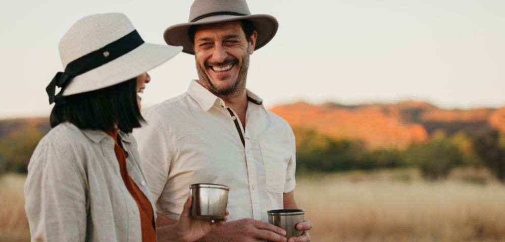 Two people outdoors, one holding a drink, with a scenic natural landscape in the background.