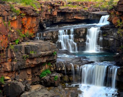 Multi-tiered waterfall cascading over rocky ledges surrounded by lush greenery.