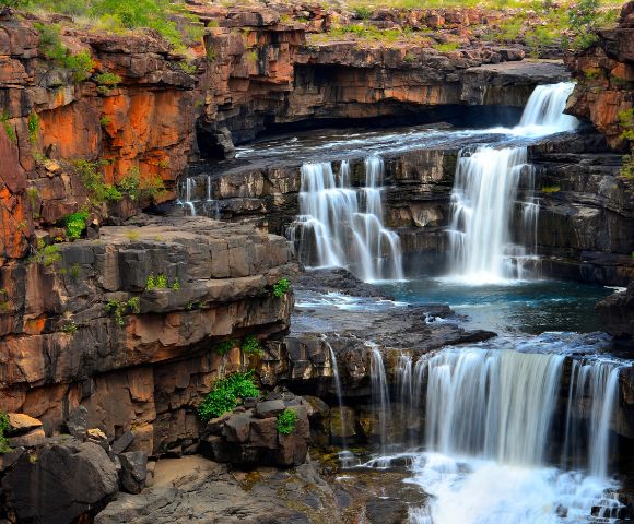 Multi-tiered waterfall cascading over rocky ledges surrounded by lush greenery.