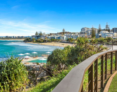 The image features a beautiful beach scene with a boardwalk overlooking the ocean. The boardwalk is lined with several umbrellas, providing shade for beachgoers. There are at least 13 umbrellas visible, scattered along the boardwalk at various distances from the water.