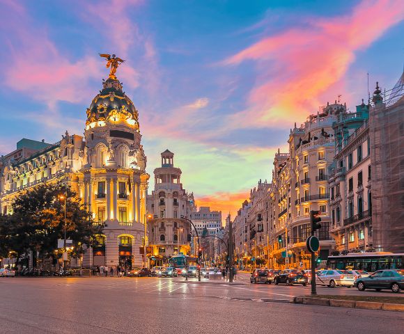 Madrid Cityscape: A sunset view of Madrid, Spain, featuring an ornate historic building and a lively street filled with people and vehicles.