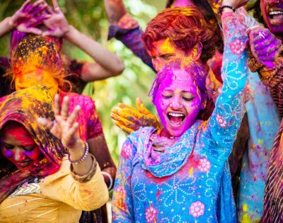 A joyful group celebrates Holi, with vibrant colors on their faces and clothes. Smiling people, lively gestures, and bright powders convey excitement.