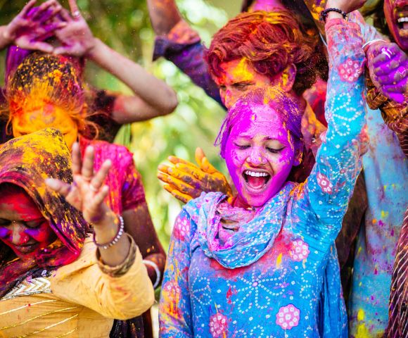 A joyful group celebrates Holi, with vibrant colors on their faces and clothes. Smiling people, lively gestures, and bright powders convey excitement.
