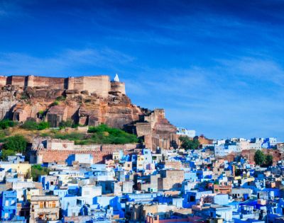Fortress atop a hill overlooks a city of blue buildings under a vibrant blue sky. The scene conveys a historic and tranquil atmosphere.