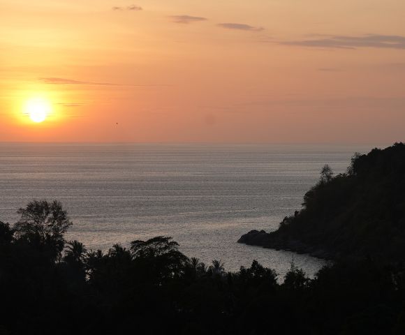 A serene sunset over calm waters, with silhouetted trees and a distant shoreline, creating a peaceful coastal scene.