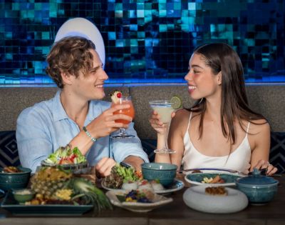 Two people enjoy food and drinks at a table, smiling warmly at each other.