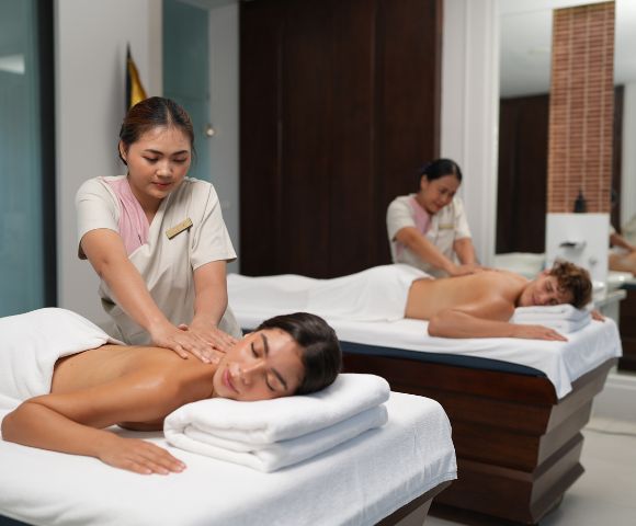 Two people receive massages on side-by-side tables in a serene indoor spa.