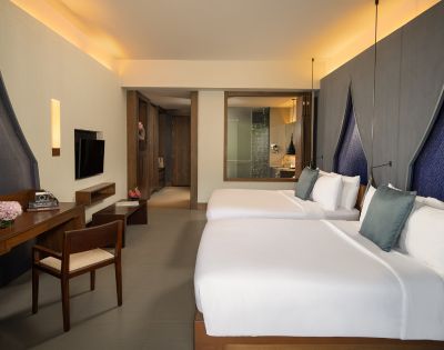 Spacious hotel room featuring two beds, a modern desk, TV, and an ensuite bathroom, with soft lighting and elegant decor.