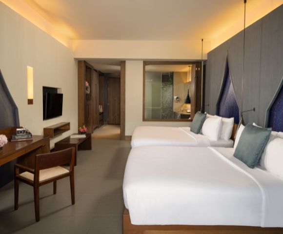 Spacious hotel room featuring two beds, a modern desk, TV, and an ensuite bathroom, with soft lighting and elegant decor.