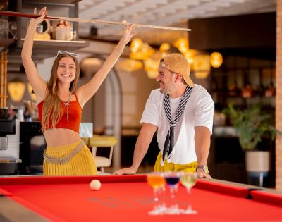 Couple behind a bar counter; one is pouring a drink while the other smiles at the camera.