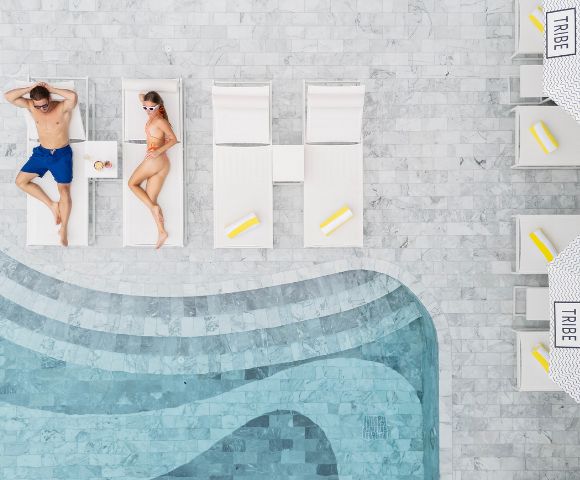Two people relax by a pool—one lounging on a sunbed and the other in the water.