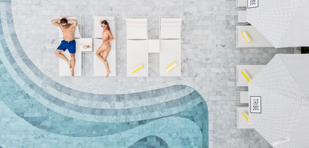 Two people relax by a pool—one lounging on a sunbed and the other in the water.