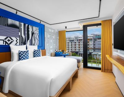 Hotel room with a large bed, blue accent wall, and floor-to-ceiling windows opening to a balcony.