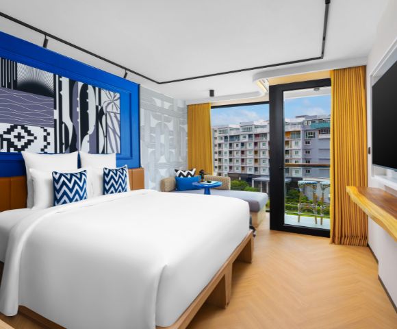 Hotel room with a large bed, blue accent wall, and floor-to-ceiling windows opening to a balcony.