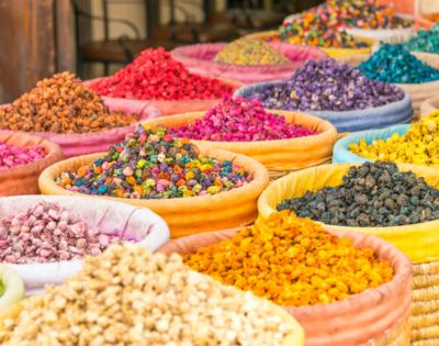 Vibrant display of colorful spices in open baskets at a market. Bright reds, purples, yellows, and blues create a lively and aromatic atmosphere.