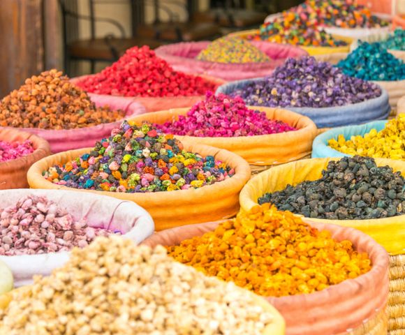 Vibrant display of colorful spices in open baskets at a market. Bright reds, purples, yellows, and blues create a lively and aromatic atmosphere.