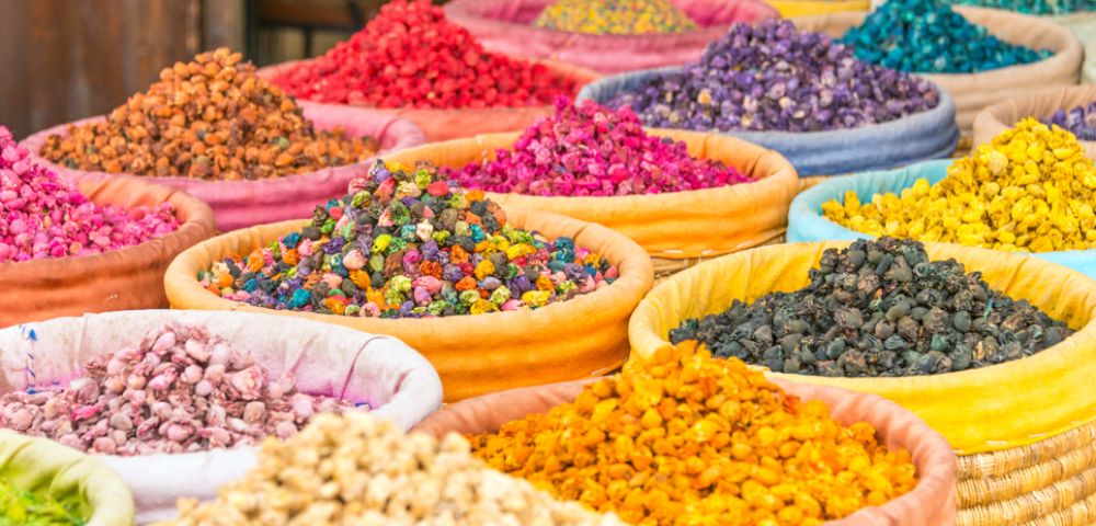 Vibrant display of colorful spices in open baskets at a market. Bright reds, purples, yellows, and blues create a lively and aromatic atmosphere.