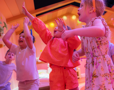 A group of children joyfully dancing and celebrating in a colorful, vibrant room filled with playful decorations.
