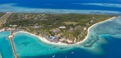 Aerial view of a tropical island with lush greenery, white sandy beaches, and turquoise waters, dotted with boats in the bay.