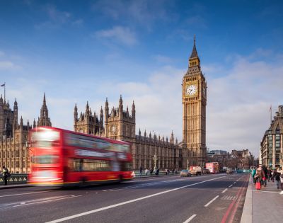 A red double-decker bus speeds past Big Ben and the Houses of Parliament in London.
