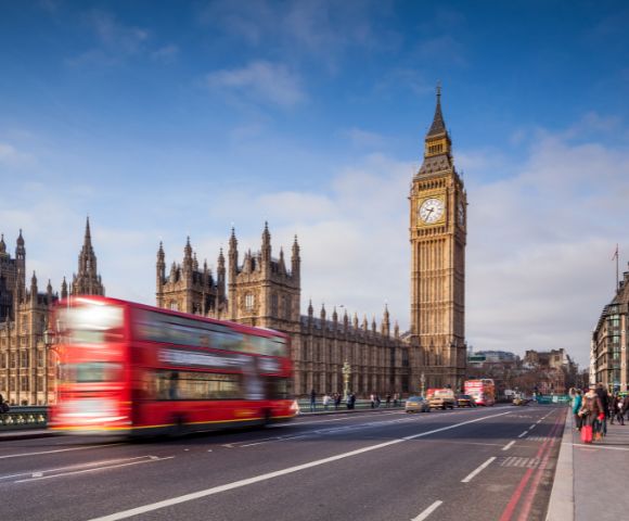 A red double-decker bus speeds past Big Ben and the Houses of Parliament in London.