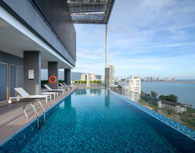 Rooftop infinity pool overlooking the city, with lounge chairs and a bright sky.