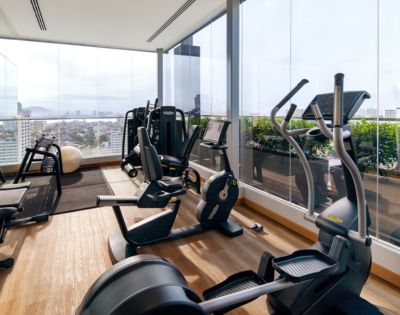 Hotel gym equipped with various exercise machines and large windows offering city views.