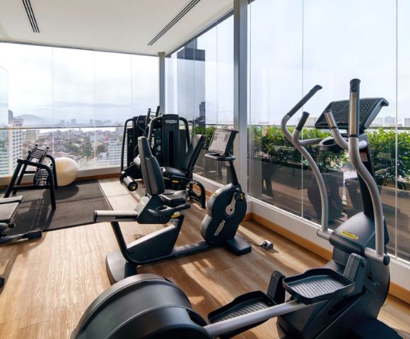 Hotel gym equipped with various exercise machines and large windows offering city views.