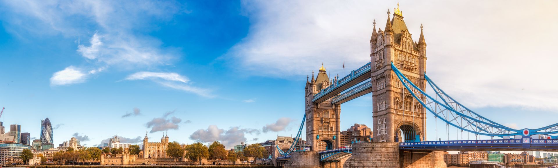 Panoramic view of Tower Bridge over the River Thames, with vibrant blue sky and reflections in the water, showcasing iconic London architecture.