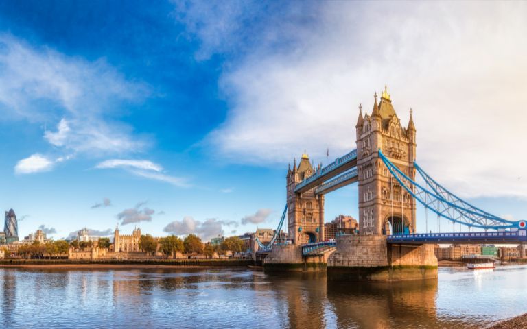 Panoramic view of Tower Bridge over the River Thames, with vibrant blue sky and reflections in the water, showcasing iconic London architecture.
