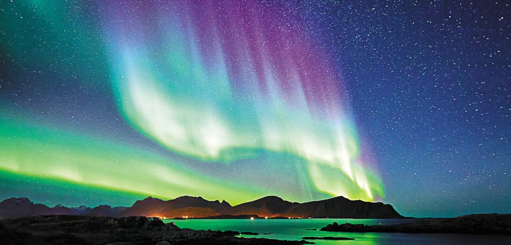 Aurora borealis illuminates the night sky above majestic mountains, creating a stunning natural spectacle.