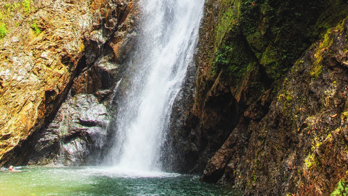 A cascading waterfall flows down rugged rocks into a serene pool, creating a tranquil and refreshing atmosphere.