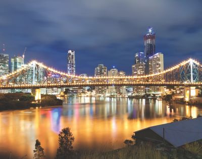 Night view of a lit bridge over water, with reflections on the surface.